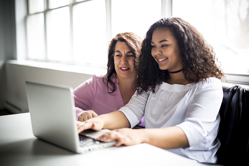 Adult mentor helping a teen mentee work on a laptop.