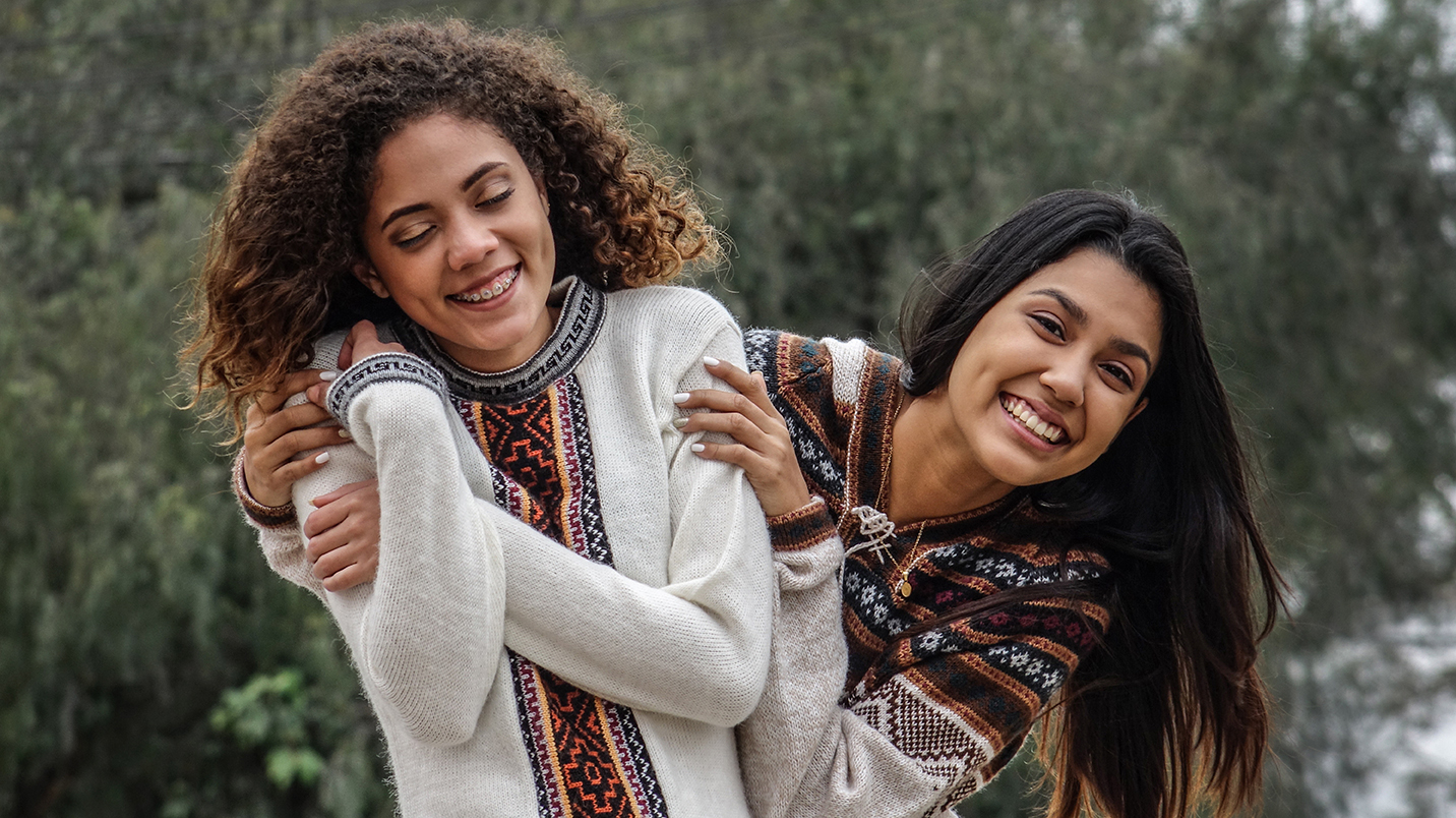 Two teenage friends playfully embrace and smile affectionately.