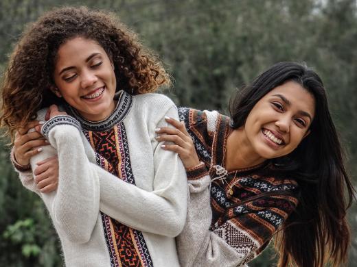 Two teenage friends playfully embrace and smile affectionately.